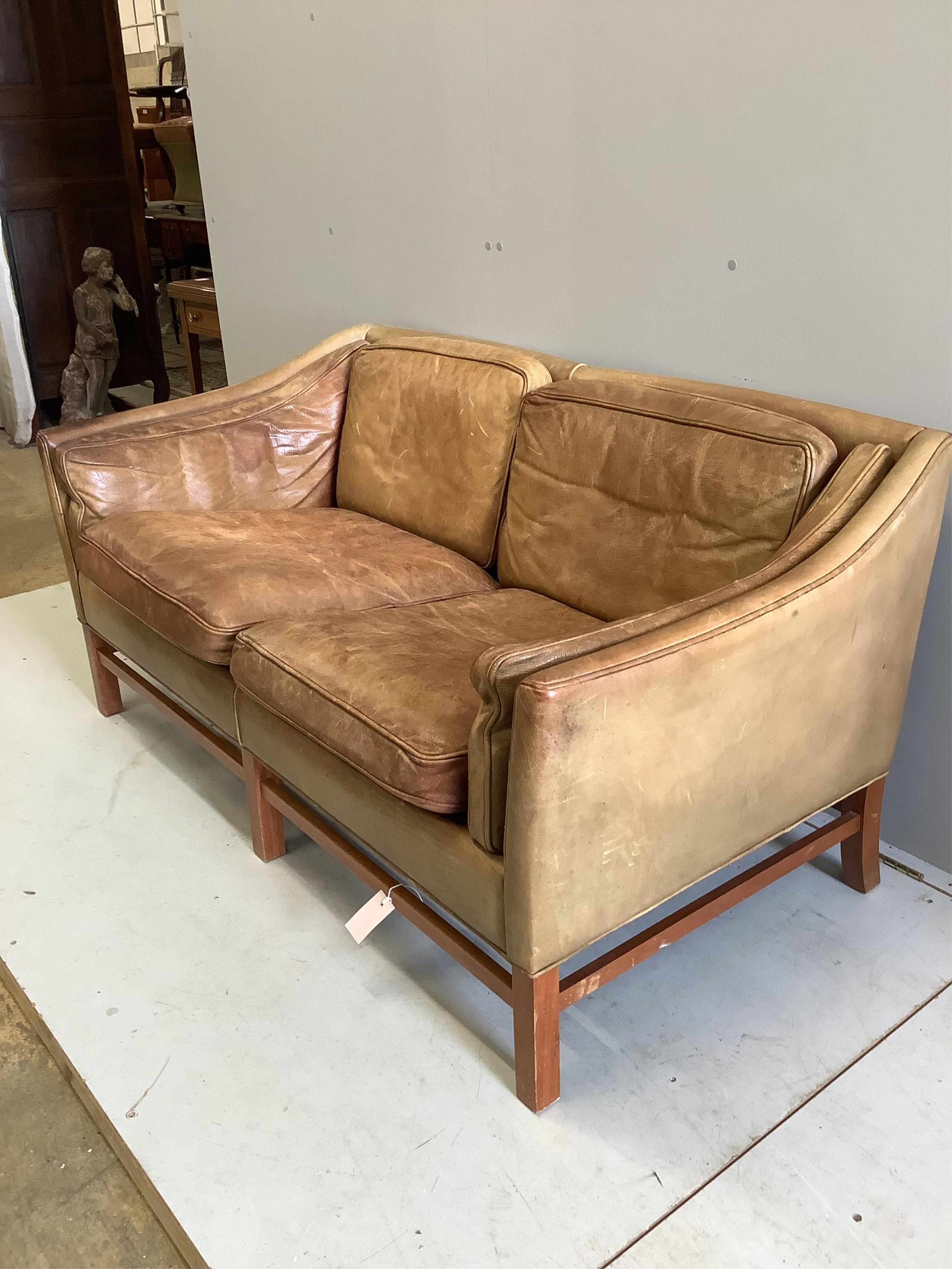 A mid century Danish teak and faded tan leather upholstered two seater settee, width 153cm. Condition - heavily faded from a light burgundy tone now down to pale tan